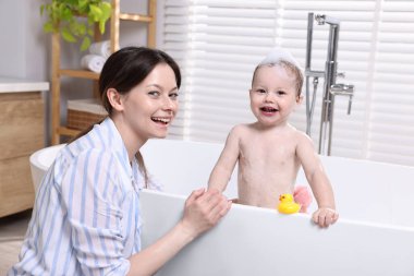 Anne küçük bebeğini küvette yıkıyor.