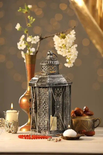 stock image Arabic lantern, misbaha, candles, dates and flowers on table against blurred lights