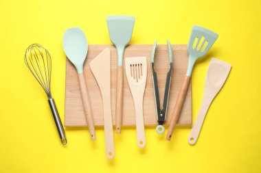 Sarı arka planda farklı spatulalar, çırpma ve maşalar, düz yatış