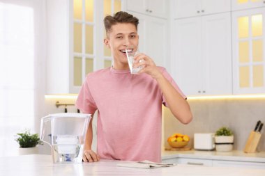 Mutfaktaki masada filtre sürahisinin yanında temiz su içen mutlu adam.