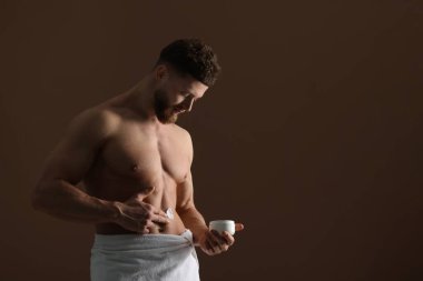 Kahverengi arka planda vücuduna nemlendirici krem süren yakışıklı bir adam.