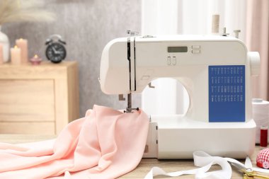 Beyaz dikiş makinesi, kumaş ve el işi aksesuarlar kapalı masa üzerinde.