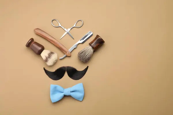 Artificial moustache and barber tools on beige background, flat lay. Space for text