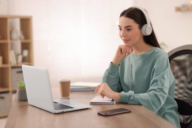 Kulaklıklı genç bir kadın masadaki Webinar 'ı izliyor.