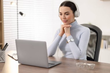 Kulaklıklı genç bir kadın ofiste Webinar izliyor.