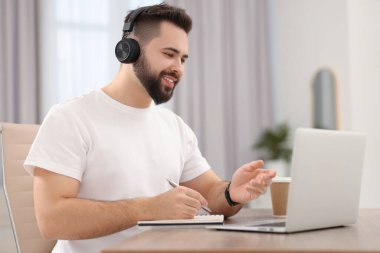 Kulaklıklı genç adam masadaki Webinar sırasında görüntülü konuşma yapıyor.