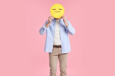 Pembe arka planda ağzı ve gözleri kapalı bir ifade tutan adam.