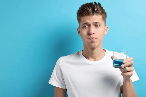 Junger Mann Benutzt Mundwasser Auf Hellblauem Hintergrund lizenzfreie Stockbilder