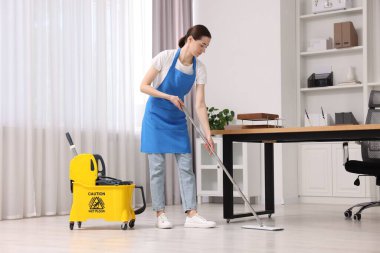Temizlik servisi. Ofiste yerleri paspasla silen bir kadın.