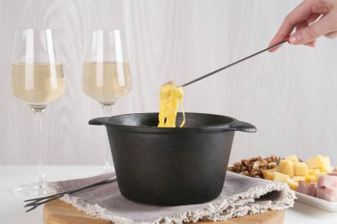 Bir parça jambonu fondü kabına daldırıp masada erimiş peynirle, yakın plan.