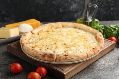 Lezzetli peynirli pizza ve malzemeler koyu gri masada.