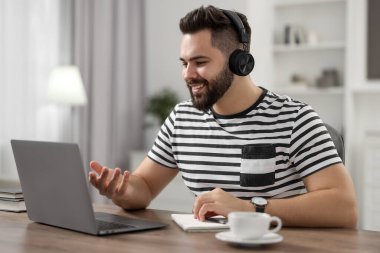 Kulaklıklı genç adam masadaki Webinar sırasında görüntülü konuşma yapıyor.