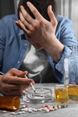 Alkol ve uyuşturucu bağımlılığı. Sigarası, viskisi ve hapları gri dokuma masasında olan adam.