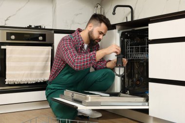 Tamirci mutfakta bulaşık makinesinin yanında kanal filtresi tutuyor.