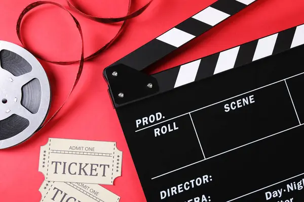 Clapperboard, movie tickets and film reel on red background, flat lay