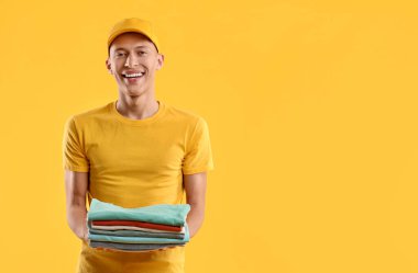 Kuru temizleme. Portakal rengi arka planda katlanmış giysiler taşıyan mutlu kurye, metin için boşluk