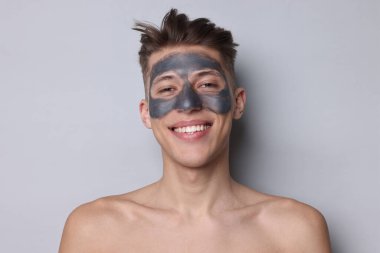 Yüzünde kil maske olan yakışıklı bir adam açık gri arka planda.