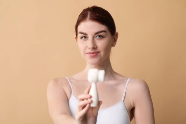 Yüzünü yıka. Bej arka planda temizlik fırçası olan genç bir kadın.