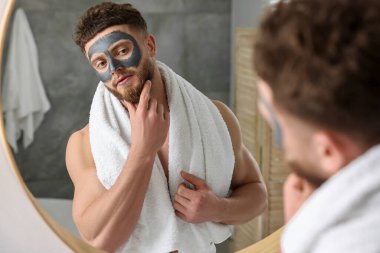 Banyoda aynanın yanında yüzü kilden maskeli yakışıklı bir adam.