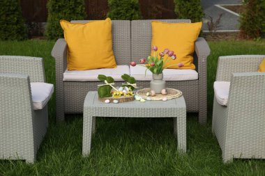 Paskalya süsleri. Vazodaki lale buketi, tavşan figürleri ve arka bahçedeki masada süslü yumurtalar.