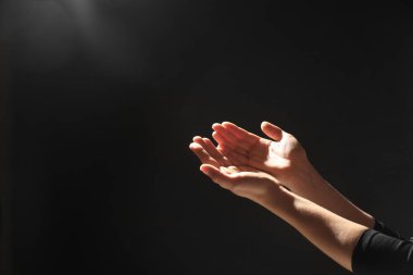 Din. Avuç içi açık bir kadın siyah arka planda dua ediyor, yakın plan. Metin için boşluk