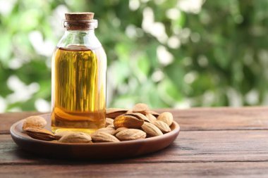 Badem yağı şişede ve fındıklar ahşap masada bulanık yeşil arka planda, yakın plan. Metin için boşluk