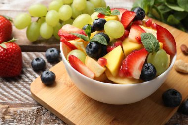 Lezzetli meyve salatası kasede ve ahşap masada malzemeler, yakın plan.