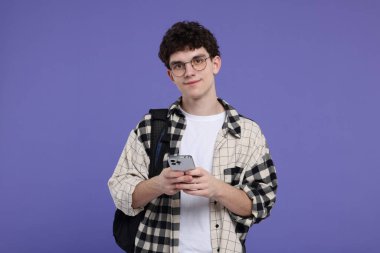 Mor arka planda sırt çantası ve akıllı telefonu olan öğrencinin portresi