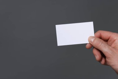 Gri arka planda boş bir kartvizit tutan adam, yakın plan. Metin için boşluk
