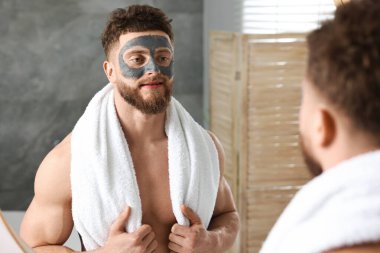 Banyoda aynanın yanında yüzü kilden maskeli yakışıklı bir adam.