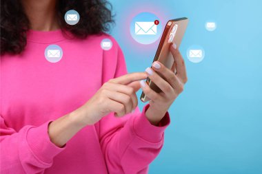 E-posta. Açık mavi arka planda cep telefonu kullanan bir kadın, yakın plan. Aygıtın etrafındaki harf çizimleri