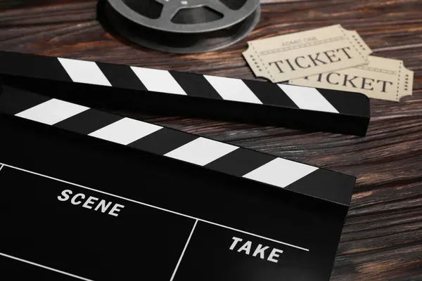 stock image Clapperboard, movie tickets and film reel on wooden table, closeup