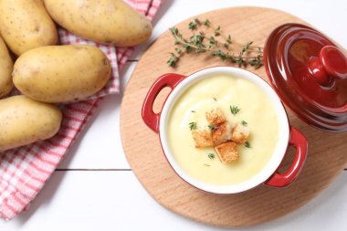 Lezzetli patates çorbası seramik çömlekte kızarmış ekmek ve beyaz ahşap masada malzemeler.