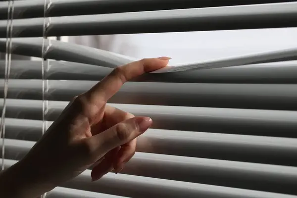 stock image Woman separating slats of white blinds indoors, closeup