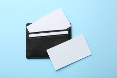 Açık mavi zemin üzerinde boş kartları olan deri kartvizit sahibi, üst görünüm