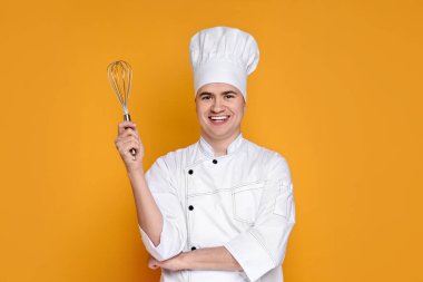 Turuncu arka planda çırpıcı tutan üniformalı mutlu bir şekerci portresi.