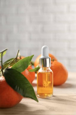 Bir şişe mandalina yağı ve beyaz ahşap masada taze meyveler.