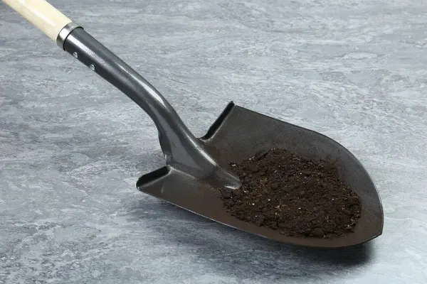 Gri desenli yüzeyinde verimli toprak bulunan metal kürek.