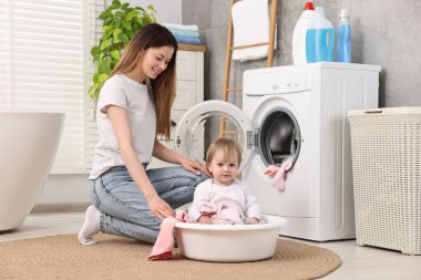 Mutlu anne kızıyla banyoda bebek kıyafetlerini yıkarken eğleniyor.