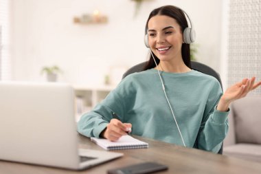 Odadaki Webinar sırasında video sohbet kullanan kulaklıklı genç bir kadın.