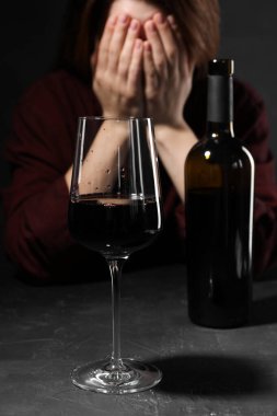 Alkol bağımlılığı. Yüzünü koyu dokulu masaya kapatan kadın, bir bardak kırmızı şaraba odaklanıyor.