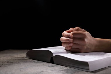 Din. Hıristiyan bir kadın siyah arka plan karşısında İncil için dua ediyor, yakın plan. Metin için boşluk