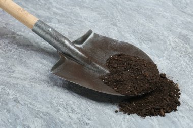 Gri desenli yüzeyinde verimli toprak bulunan metal kürek.