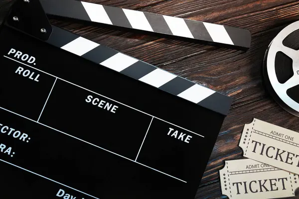 stock image Clapperboard, movie tickets and film reel on wooden table, flat lay