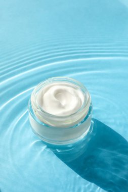 Açık mavi arkaplandaki suda nemlendirici kremalı kavanoz.