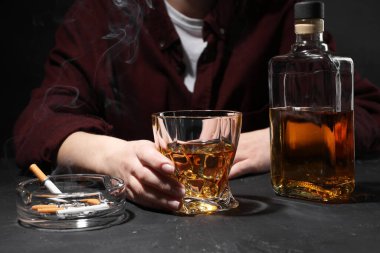 Alkol bağımlılığı. Viski ve sigara içen kadın koyu dokulu masada, yakın plan.