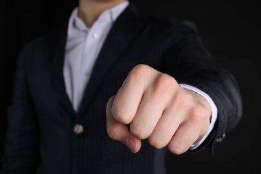 Siyah arka planda dövmesi olan bir iş adamı yumruğunu gösteriyor.