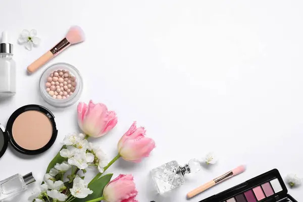 Flat lay composition with different makeup products and beautiful spring flowers on white background, space for text