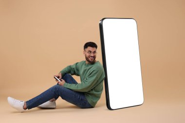 Cep telefonu olan bir adam koyu bej arka planda boş ekranı olan büyük bir cihazın yanında oturuyor. Tasarım için model