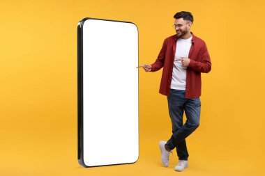 Adam turuncu arka planda boş ekranı olan büyük bir cep telefonunu işaret ediyor. Tasarım için model